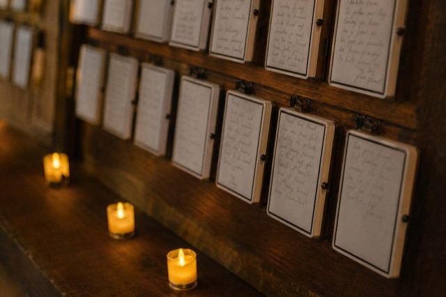 Close-up of a wall of prayer cards on small e-ink panels arranged like paper cards on a wooden frame, candles glowing below.